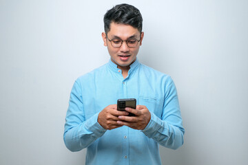 Smiling young good looking Asian man using smartphone to get in touch with family and friends isolated