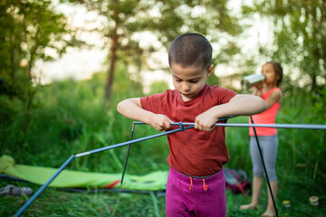 Wall Mural - Little boy assembling racks of tent in camp on summer sunset in forest outdoors