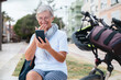 © luciano - Handsome caucasian senior woman casual dressed sitting outdoors close to her bicycle using mobile phone in chat