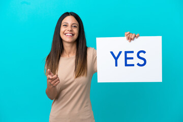 Wall Mural - Young woman over isolated background holding a placard with text YES and pointing it