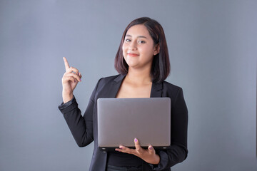 Mexican woman smiling holding laptop and pointing on gray background