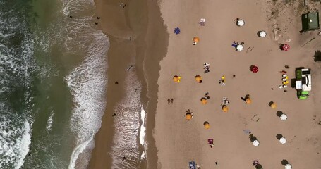 Wall Mural - Summer day at a local beach with people relaxing under umbrellas and waves breaking.