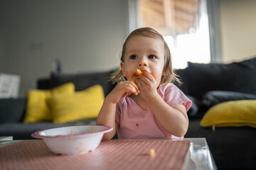 one girl small caucasian toddler female child daughter eating alone at the table at home while watching tv making mess on her face dirty sauce childhood growing up development concept copy space