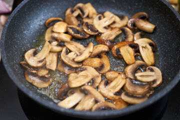 Sliced mushrooms in a frying pan on induction hob at domestic kitchen