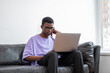 Black man with laptop sitting on couch, pensive look