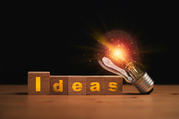 Wall Mural - Glowing lightbulb with Ideas wording on wooden cube block for creative thinking idea and knowledge concept.