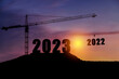 Silhouette of engineer and construction to create lifting crane 2023 on blue sky background.