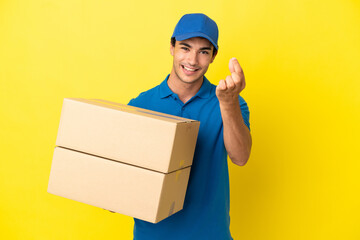 Wall Mural - Delivery man over isolated yellow wall making money gesture