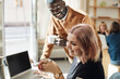 © Maskot - Side view of smiling female entrepreneur holding coffee cup by with colleague in office