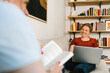 © Maskot - Smiling lesbian woman freelancing on laptop while talking with girlfriend in living room