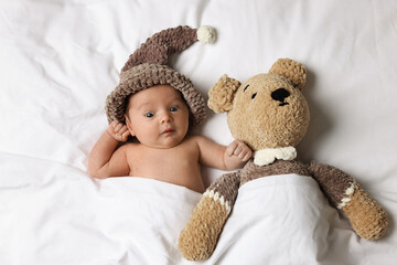 Canvas Print - Cute little baby with toy bear lying under blanket in bed, top view