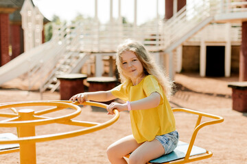 A charming little girl is walking in the park, swinging on a swing. Happy childhood, playtime