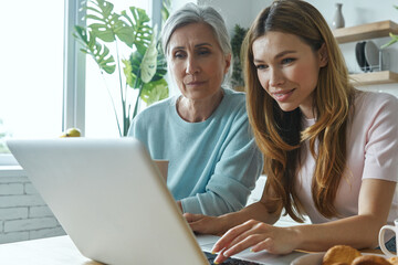 Wall Mural - Senior woman and her adult daughter using laptop while spending time at home together