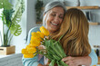 Leinwandbild Motiv Joyful senior woman embracing her daughter and holding a bunch of yellow tulips