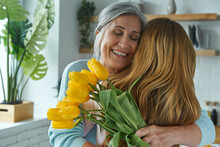 Joyful Senior Woman Embracing Her Daughter And Holding A Bunch Of Yellow Tulips