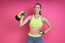 Happy Young Woman In Sports Clothing Carrying Kettlebell Against Pink Background
