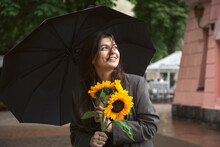 A Young Woman With A Bouquet Of Sunflowers Under An Umbrella In Rainy Weather.