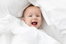 Laughing Newborn Baby Peeking From White Sheet