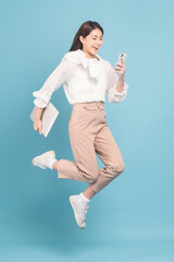 Wall Mural - Young beautiful asian woman with smart casual cloth use smartphone and jump isolated on blue background