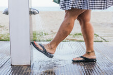 Unrecognizable Woman With Varicose Veins On Her Legs Washes Sand From Her Feet And Sandals In The Shower At The Beach