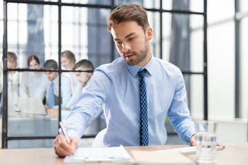 Wall Mural - Young man is working with papers while sitting in the office. Successful entrepreneur is studying documents with attentive and concentrated look.