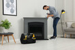 © New Africa - Man sealing electric fireplace with caulk near wall in room