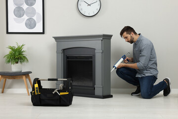 Poster - Man sealing electric fireplace with caulk near wall in room