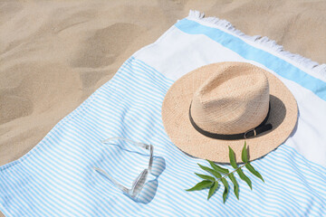 Wall Mural - Beach towel with straw hat, sunglasses and leaves on sand