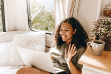 Side View Of African American Woman On White Sofa In Her Camper During Road Trip On Weekends, Greeting Parents While Having Online Video Chat, Using Wireless Conncection. People And Technology Concept