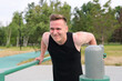 © Евгений Шемякин - Young handsome fit athletic strong man is training doing triceps and chest pull ups in park on sports ground outdoors on bar at summer. Open air gym. Bodybuilding, fitness sport healthy lifestyle.