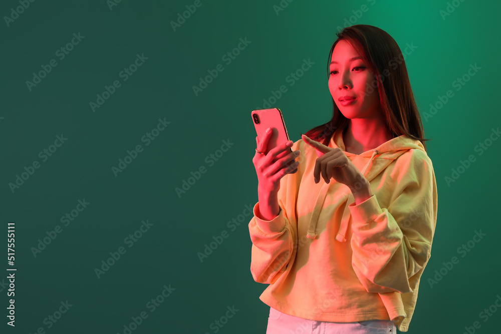 Female Asian blogger with smartphone on green background