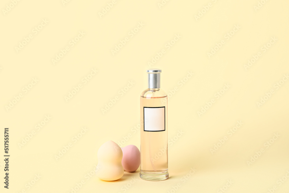 Bottle of perfume and makeup sponges on color background
