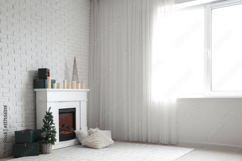 Electric fireplace with candles, gift boxes and Christmas tree near white brick wall