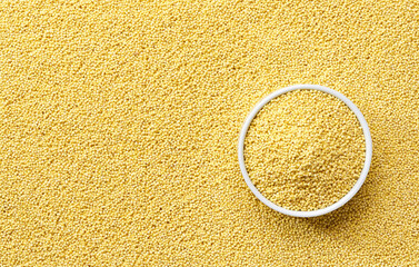 ceramic plate with dry millet groats on a millet yellow grains background close-up top view.