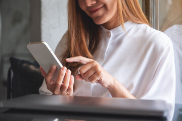 Wall Mural - Closeup image of a young woman holding and touching on mobile phone screen with laptop on the table