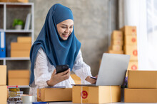 Muslim Young Asian Woman Working At Home Doing Sme Ecommerce Online Small Business Entrepreneur Checking Postal Parcels To Delivery To Online Customers, Startup Muslim Sme Business Concept.