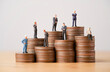 Many Business miniature figure standing on coins stacking for different income and salary in each position.