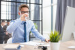 © ty - Handsome businessman using PC and drinking water in office area with collegues on the background