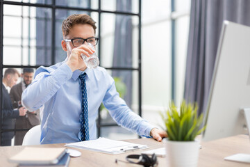 Sticker - Handsome businessman using PC and drinking water in office area with collegues on the background