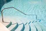 Fototapeta  - Steps going into aqua blue swimming pool with metal hand rail 