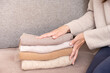 Female hands stack cozy knitted sweaters on the sofa. Warm concept