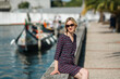 © De Visu - A woman sits a canal promenade in Aveiro, Portugal. Traditional boats in the background are in a blur.