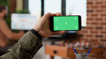 Poster - Business manager holding horizontal greenscreen on smartphone, looking at blank chroma key copyspace on display. Using isolated mockup template or background on telephone. Close up.