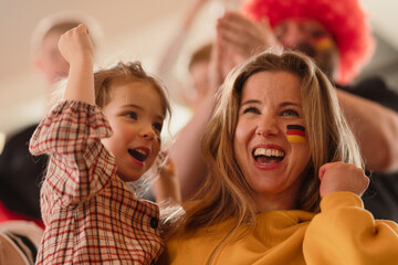 Excited football fans, mother with little daughter, supproting German national team in live soccer match at stadium.