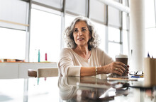 Senior Businesswoman With Coffee Cup Sitting At Desk