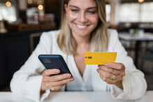 Smiling Businesswoman Holding Credit Card Doing Online Shopping Through Smart Phone At Restaurant