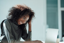 Happy Businesswoman With Hand In Hair Using Laptop At Office