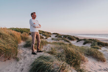 Happy Man With Arms Crossed Standing On Sand Dune At Beach