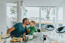 Father Kissing Son Sitting At Dining Table