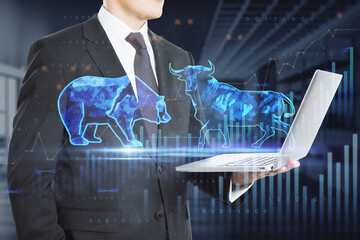 Poster -  bulls and bears struggle. Equity market illustration. Close up of businessman hand holding laptop with creative hologram and graph on blurry office interior background. Double exposure.